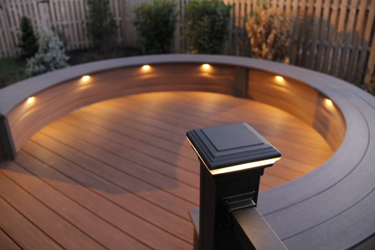 Recessed deck lights washing a curved bench cap at dusk, with a lighted post cap in the foreground