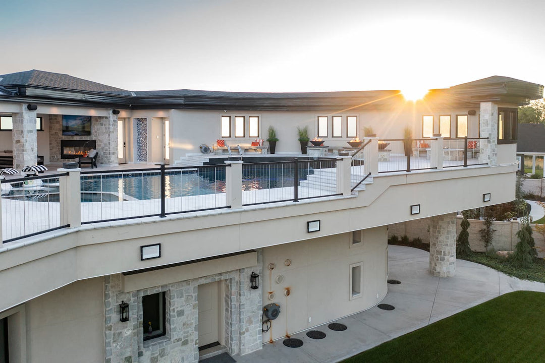 Modern two-story residential house exterior at sunset with a large wraparound deck, vertical cable railings.