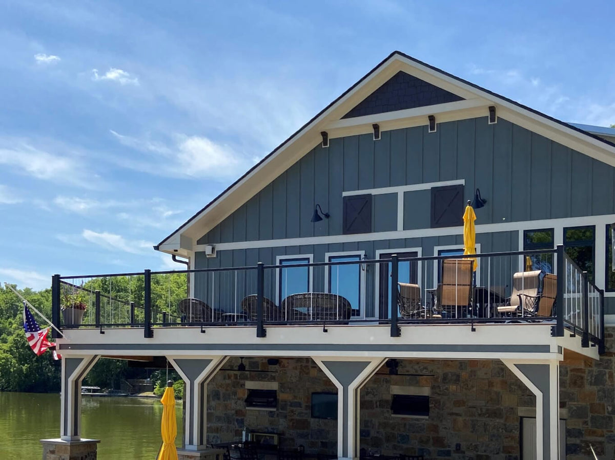 Keylink horizontal cable railing on textured black fascia mount posts, hanging off the deck frame of a lakeside home